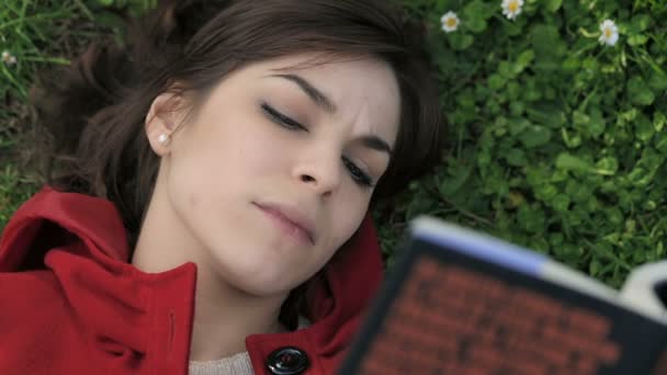 Schönes Mädchen liest Buch im Gras liegend: Park, Frühling, im Freien — Stockvideo