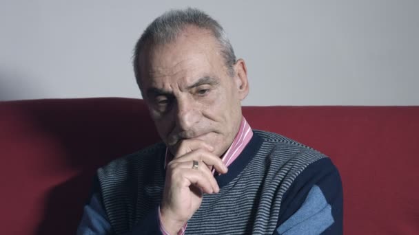 Застенчивый старик, сидящий один дома на красном диване — стоковое видео