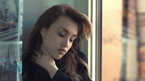 Вдумчивая и проблемная женщина массирует шею у окна — стоковое видео