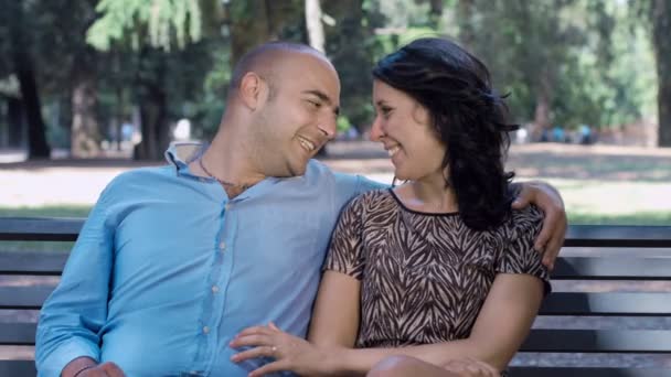 Влюбленные целуются сидя на скамейке в общественном парке: влюбленная пара — стоковое видео