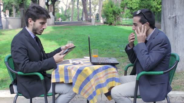 Два бизнесмена смотрят на планшет и ноутбук во время бизнес-завтрака — стоковое видео