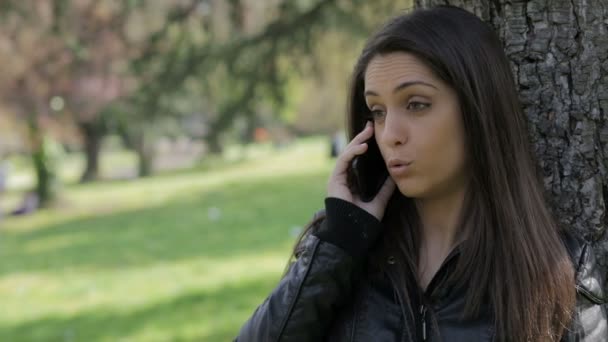 Menina bonito está tendo chamada no parque: smartphone: celular, telefone celular, ao ar livre — Vídeo de Stock