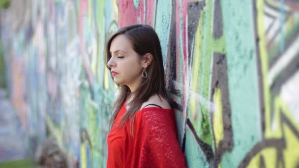 Mujer triste con una camisa roja está llorando apoyada en una pared pintada con murales — Vídeos de Stock