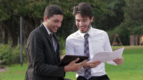 Two young businessmen with tablet computer talk about a project on a park — Stock Video