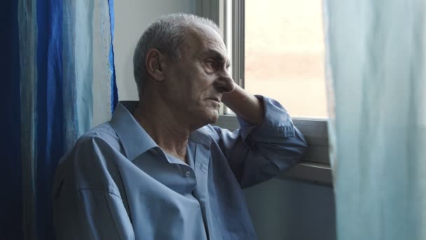 Oude man is denken aan iets ergs zitten alleen in de buurt van het venster — Stockvideo