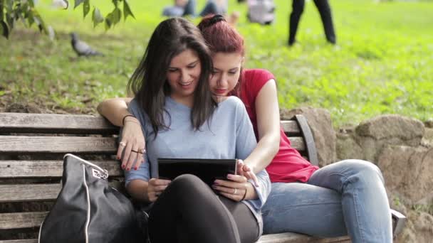 Dwie dziewczyny za pomocą tabletu na ławce w parku — Wideo stockowe