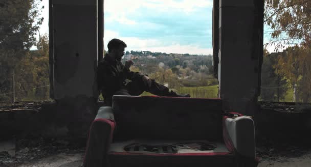 Солдат сидит на подоконнике окна, курит сигару в заброшенном здании — стоковое видео