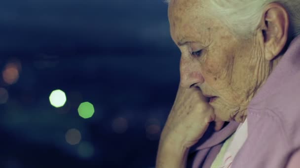 Nadenkend en depressief oude vrouw kijkt uit raam in de nacht — Stockvideo