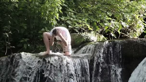 Een man wast in een rivier met watervallen — Stockvideo