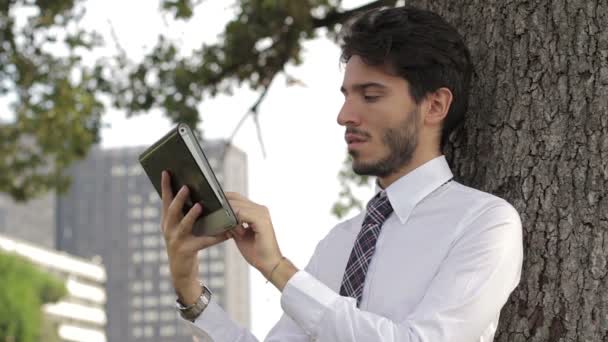 Joven hombre de negocios bajo el árbol usando tableta — Vídeo de stock