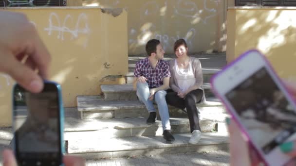 Двое влюбленных фотографируются с друзьями - мобильный телефон - поцелуй - фото — стоковое видео