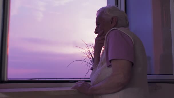 Anciana solitaria mirando por la ventana al atardecer — Vídeos de Stock