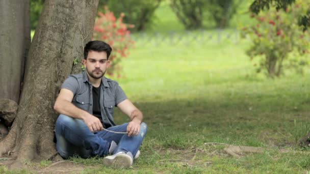 Amigos consuelan a un joven sentado deprimido y triste cerca de un árbol en un parque — Vídeo de stock