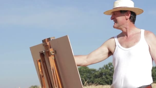 Schilder in het midden van een tarweveld schildert een prachtig landschap, Pan — Stockvideo