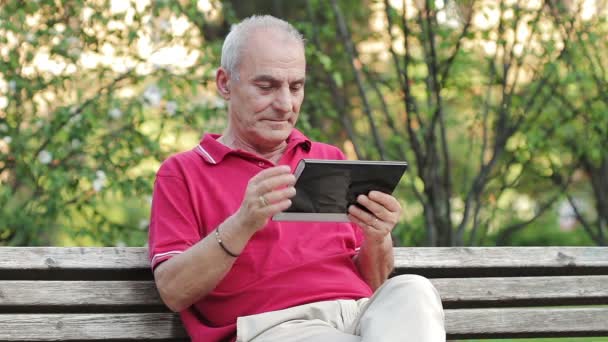 Пенсионер отдыхает и пользуется планшетом за столом в парке — стоковое видео