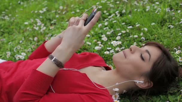 Красива дівчина використовує смартфон в парку: слухати музику, на відкритому повітрі, брехати — стокове відео
