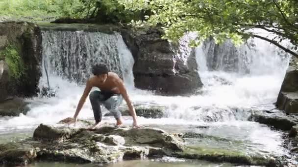 Хлопчик перетнув струмок, щоб сидіти на скелі — стокове відео