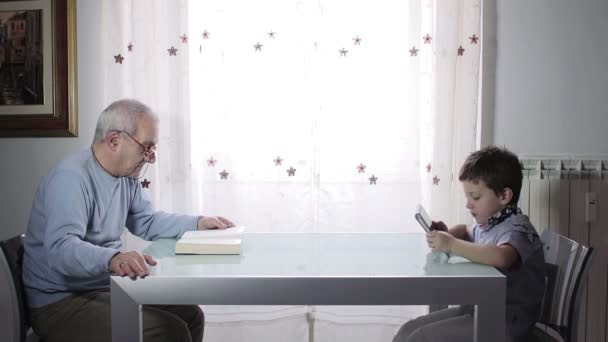 Abuelo leyendo un libro mientras el bebé juega con una tableta - antiguo vs moderno — Vídeos de Stock