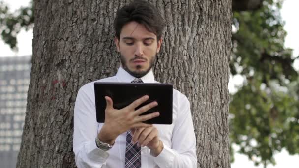 Joven hombre de negocios bajo el árbol usando tableta — Vídeos de Stock