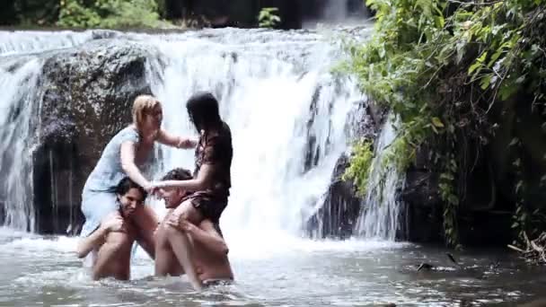 Niños y niñas se están divirtiendo en un lago, luchando y salpicando con agua — Vídeo de stock