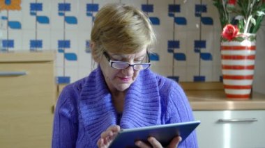 Mutfakta tablet bilgisayar kullanan yaşlı kadın: facebook, twitter, posta, web