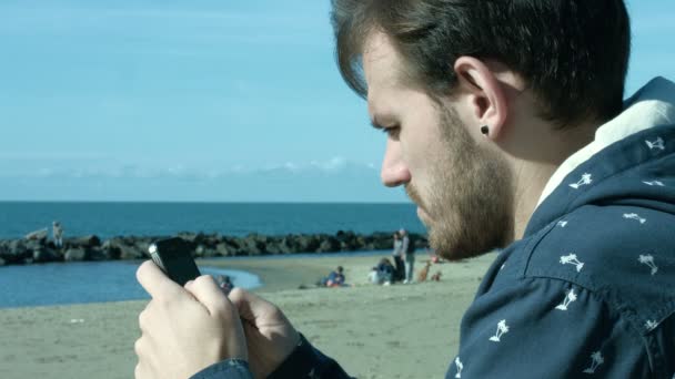 Hombre usando el teléfono inteligente cerca del mar en el invierno — Vídeos de Stock