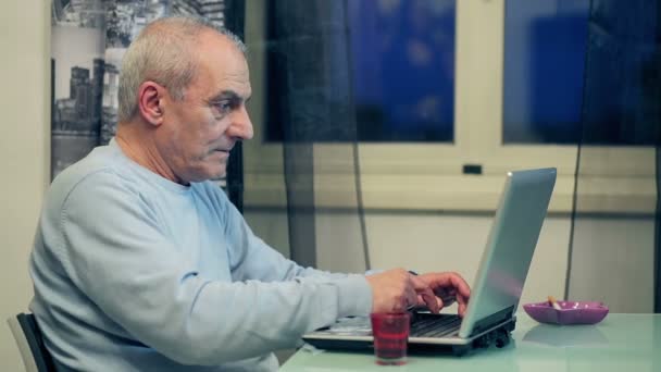 Пожилой человек изучает компьютер и пьет кофе — стоковое видео