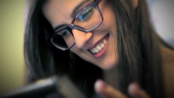 Счастливая молодая женщина с очками, сидящая в баре и пользующаяся планшетным компьютером — стоковое видео