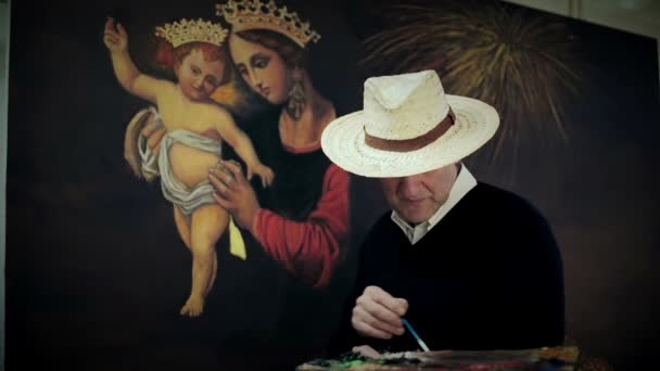 Artista pintor posando con sombrero blanco delante de su pintura. Está mirando la cámara. — Vídeo de stock