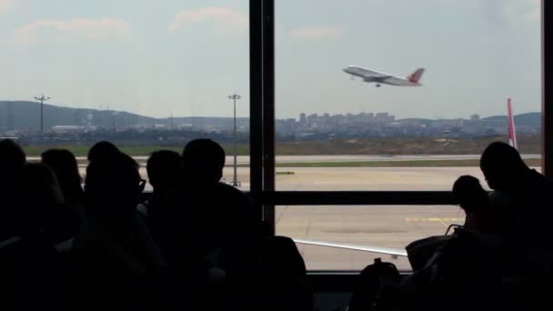 Personas esperando en la terminal del aeropuerto con aviones despegando en el fondo — Vídeo de stock