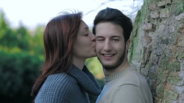Aranyos lány megcsókolja a csinos, fiatal férfi, támaszkodva egy fa: szerelem, móka, ifjúsági — Stock videók