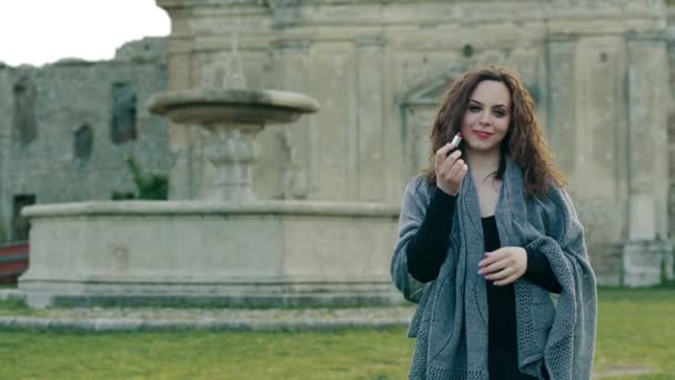Porträt einer verrückten Frau allein im antiken Park, während sie roten Lippenstift auf die Lippen legt — Stockvideo
