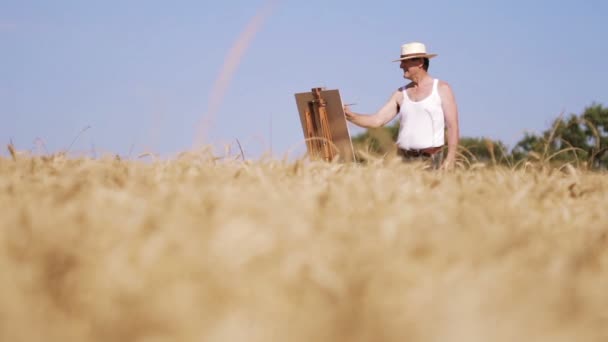 Живописец посреди пшеничного поля рисует красивый пейзаж, холст — стоковое видео