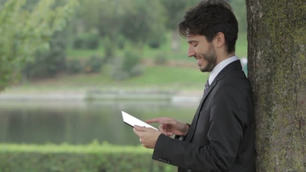 Joven hombre de negocios bajo el árbol usando tableta — Vídeo de stock