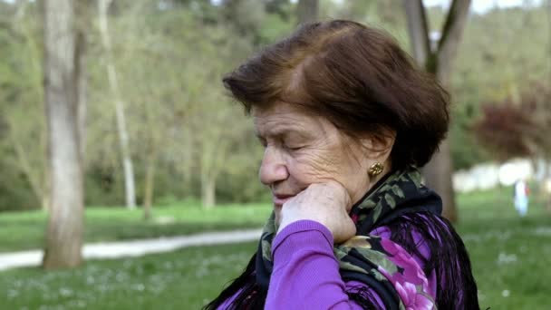 Sad and depressed lonely old woman is sitting in a public park — Stock Video