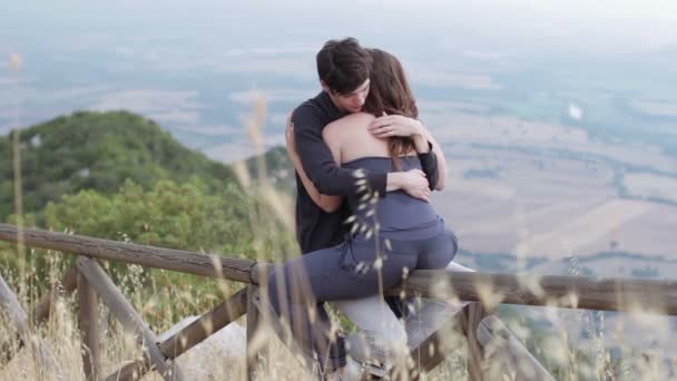 Un chico en una valla en la montaña abrazando a su novia y la besa — Vídeos de Stock