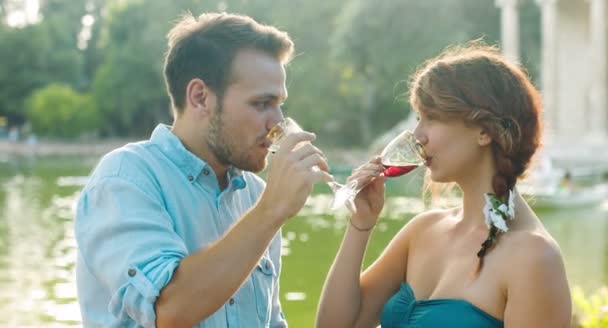 Pareja romántica enamorada haciendo un brindis cerca de un pequeño lago: amor, cita, bebida — Vídeo de stock