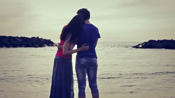 A boy on the seashore at sunset hugs her girlfriend and jokes  with water — Stock Video