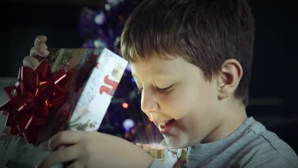 Verbaasd en opgewonden kind opent een doos met een gift van Kerstmis — Stockvideo