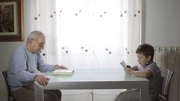 El pasado y el futuro, abuelo leyendo un libro y el niño utiliza tableta — Vídeo de stock