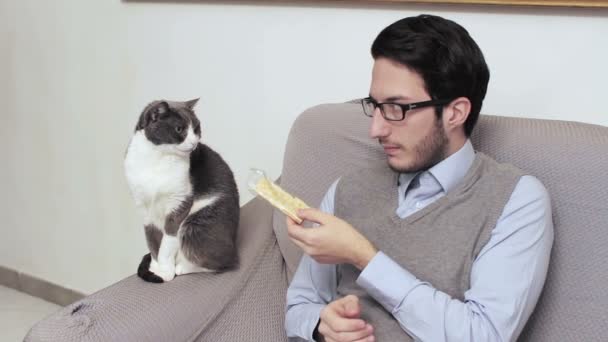 Niezdarny młody człowiek, jedząc krakersy i oferuje je do kota — Wideo stockowe
