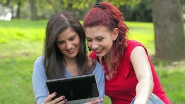 Birlikte bir tablet pc kullanarak yeşil çimenlerin üzerinde oturan lezbiyenler