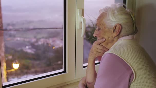 Nadenkend en trieste oude vrouw kijkt uit raam bij zonsondergang — Stockvideo