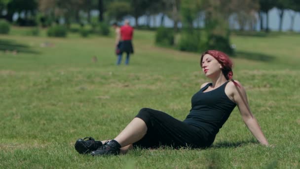 Красивая рыжая женщина расслабляется сидя на лугу — стоковое видео