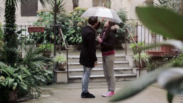 Primer beso - un hombre besa a una mujer bajo un paraguas bajo la lluvia — Vídeo de stock