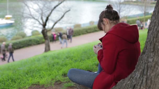 Menina bonita usando smartphone no parque: sentado, sozinho, feliz, mensagem — Vídeo de Stock