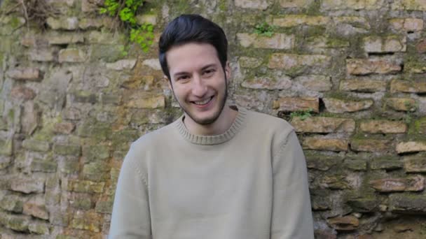 Young man smiling with a crick wall on background — ストック動画