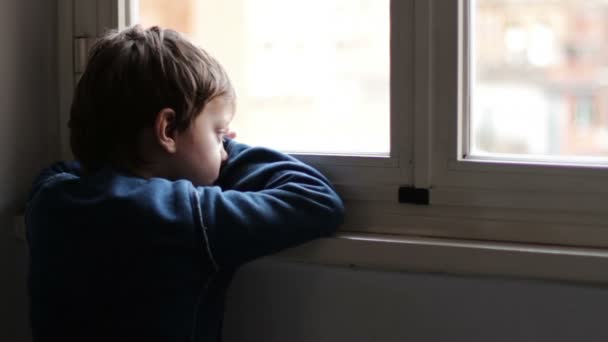 Ребенок грустный и одинокий глядя в окно — стоковое видео