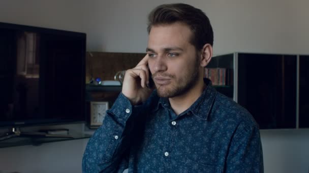 Jovem sorrindo usando smartphone; atraente, casual, em casa. Filmagem 4k — Vídeo de Stock