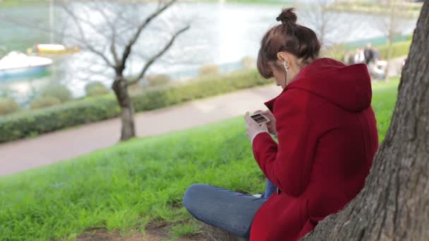 Hermosa chica usando el teléfono inteligente en el parque: mensaje, foto, búsqueda, al aire libre — Vídeos de Stock